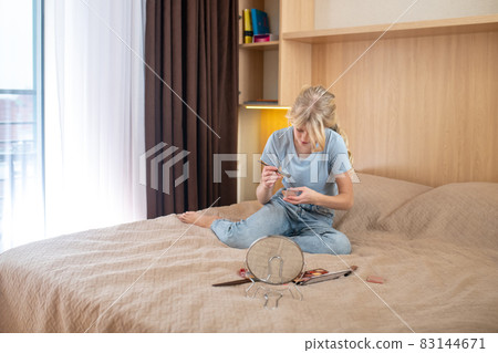 A girl in blue shirt sitting on her bed and looking in the mirror 83144671