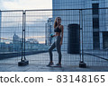 Young athletic woman in sports clothes standing with water bottle in hands on urban city location 83148165