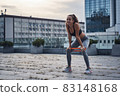 Young athletic woman smiling while doing squats exercises with sports rubber at the urban city location 83148168