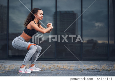 Young athletic woman doing squats exercises with sports rubber at the urban city location 83148171