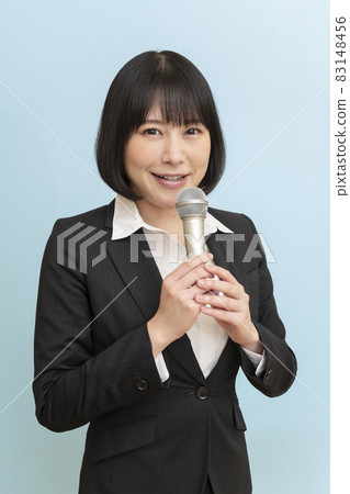 Woman holding a microphone in front of a blue wall Woman holding a microphone in front of a blue wall 83148456