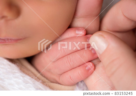 Happy mom lovingly hold the fingers of a newborn baby in a soft grey plaid Happy mom lovingly hold the fingers of a newborn baby in a soft grey plaid 83153245