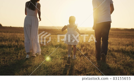 a little laughing girl runs with her parents at sunset, a happy family, a childhood dream, kid running in sunshine with mom and dad, playing catch-up with child, father and mother with baby daughter 83155655