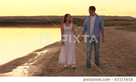 Happy man and woman walk along the beach at sunset, romantic summer trip, love of adults, good relationship of lovers, life of happy family, relaxing on the weekend in light of sun, talking together Happy man and woman walk along the beach at sunset, romantic summer trip, love of adults, good relationship of lovers, life of happy family, relaxing on the weekend in light of sun, talking together 83155658