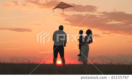 Happy family day, father mother and little kid fly a kite into the sky at sunset, play with child in nature in the evening, love spending time with family, raising and developing baby, cheerful life. Happy family day, father mother and little kid fly a kite into the sky at sunset, play with child in nature in the evening, love spending time with family, raising and developing baby, cheerful life. 83155797