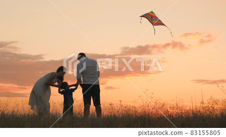 Happy family day, father mother and little kid fly a kite into the sky at sunset, play with child in nature in the evening, love spending time with family, raising and developing baby, cheerful life. Happy family day, father mother and little kid fly a kite into the sky at sunset, play with child in nature in the evening, love spending time with family, raising and developing baby, cheerful life. 83155805