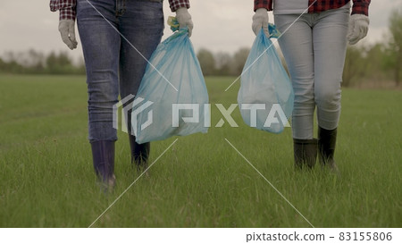 A man carries garbage in garbage bags on green grass, collection and disposal of unnecessary waste, a woman in gloves for cleaning work, help protecting the planet's environment, clean earth 83155806