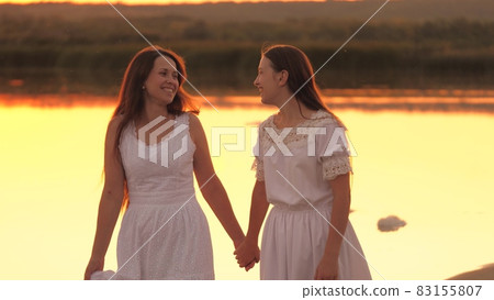 Happy girls are resting together walking along beach at sunset, traveling on vacation in rays of sun, cheerful female team, teamwork, smiles and laughter when people talk, spending time interestingly 83155807