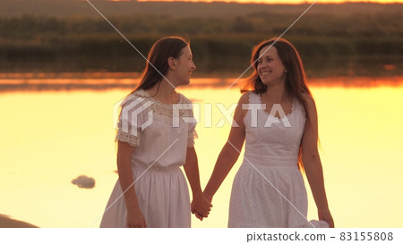 Happy girls are resting together walking along beach at sunset, traveling on vacation in rays of sun, cheerful female team, teamwork, smiles and laughter when people talk, spending time interestingly Happy girls are resting together walking along beach at sunset, traveling on vacation in rays of sun, cheerful female team, teamwork, smiles and laughter when people talk, spending time interestingly 83155808