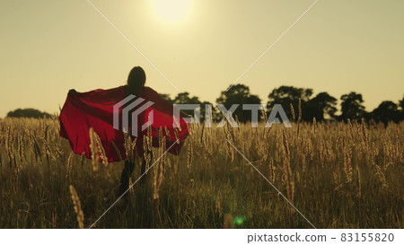A girl runs across the field in a red superhero cloak waving in the wind at sunset, childhood dream to be a strong winner, the concept of a happy man, a woman wants to save the day, slow motion A girl runs across the field in a red superhero cloak waving in the wind at sunset, childhood dream to be a strong winner, the concept of a happy man, a woman wants to save the day, slow motion 83155820