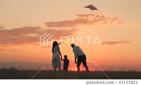 Happy family, little child with father and mother launch flying kite into sunset sky, silhouette of mom dad and kid together, flying toy flies high on his head, children's fantasy dreams, travel fun Happy family, little child with father and mother launch flying kite into sunset sky, silhouette of mom dad and kid together, flying toy flies high on his head, children's fantasy dreams, travel fun 83155822