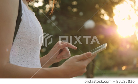 A young girl holds in her hand a modern tablet in the glare of the sunset, go online to the Internet, the rays of the sun shine on the touch screen of the tablet, the concept of modern technologies 83155836