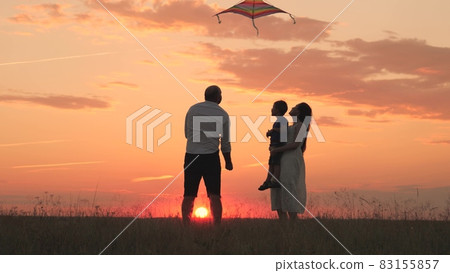 Happy family day, father mother and little kid fly a kite into the sky at sunset, play with child in nature in the evening, love spending time with family, raising and developing baby, cheerful life. 83155857
