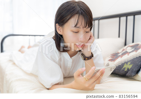 A woman lying face down on her bed and looking at her smartphone 83156594