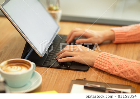 Female hands in pink sweater at cafe typing on keyboard working on modern tablet computer Female hands in pink sweater at cafe typing on keyboard working on modern tablet computer 83158354
