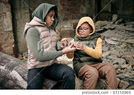 Two hungry girls sharing peach while sitting on ruins of building 83158968