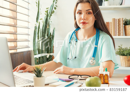 Good looking woman doctor sitting at her table in medical office Good looking woman doctor sitting at her table in medical office 83159187