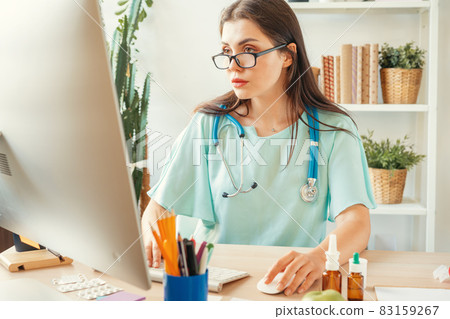 Good looking woman doctor sitting at her table in medical office Good looking woman doctor sitting at her table in medical office 83159267
