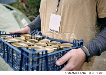 Male volunteer carrying plastic box with tinned food 83159308