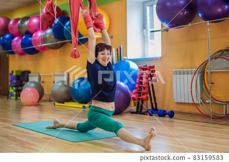 Senior mature woman practices anti-gravity yoga with a hammock in a studio. Lifestyle 83159583