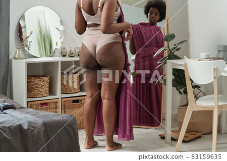 Rear view of young plus size woman trying on new dress 83159635