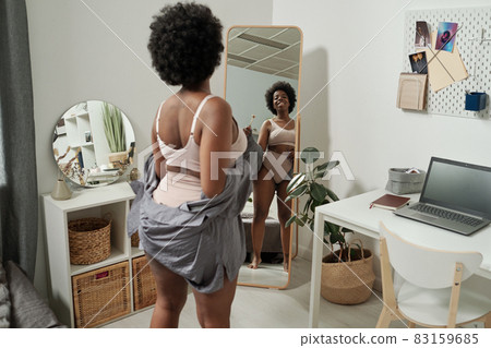 Happy young African woman in underwear looking in mirror Happy young African woman in underwear looking in mirror 83159685