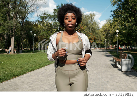 Young sportswoman with earphones jogging in park Young sportswoman with earphones jogging in park 83159832