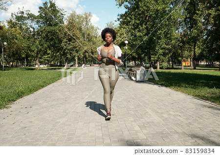 Young active plus size female jogging along road Young active plus size female jogging along road 83159834