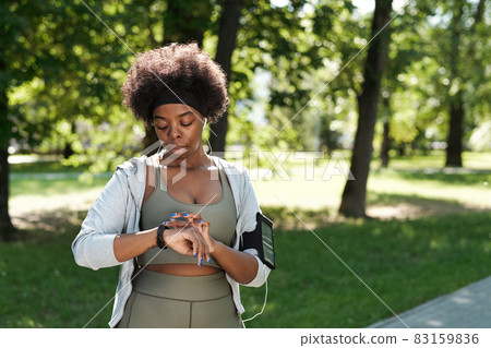 Young African woman in sportswear looking at smartwatch Young African woman in sportswear looking at smartwatch 83159836