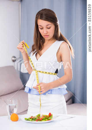 Smiling young girl is measuring the waist after healthy meal 83159839