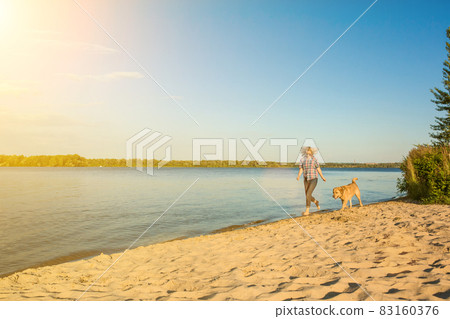 Happy young woman walking along a beach with her golden retriever at the sunset. Sun flare Happy young woman walking along a beach with her golden retriever at the sunset. Sun flare 83160376