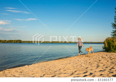 Happy young woman walking along a beach with her golden retriever at the sunset 83160377