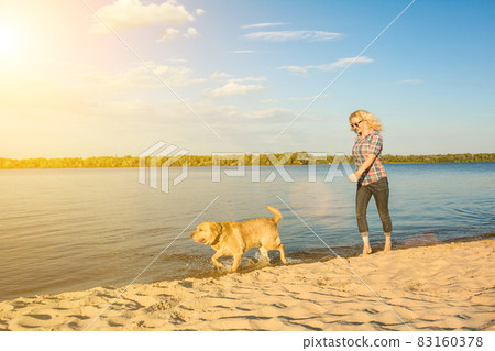 Happy young woman walking along a beach with her golden retriever at the sunset. Sun flare 83160378
