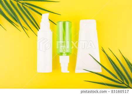 Set of cosmetic tubes with beauty products on yellow background with palm leaves 83160517
