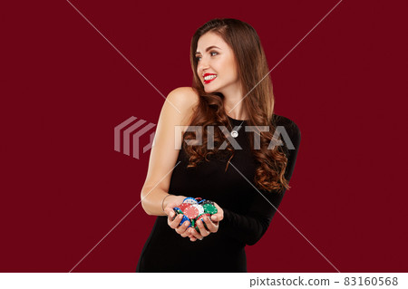 Casino, gambling, poker, people and entertainment concept - woman poker player in black dress with chips in hands on red background. Casino, gambling, poker, people and entertainment concept - woman poker player in black dress with chips in hands on red background. 83160568