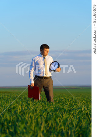 a businessman holds an office clock and red folder in a field with green grass - business and time concept a businessman holds an office clock and red folder in a field with green grass - business and time concept 83160679