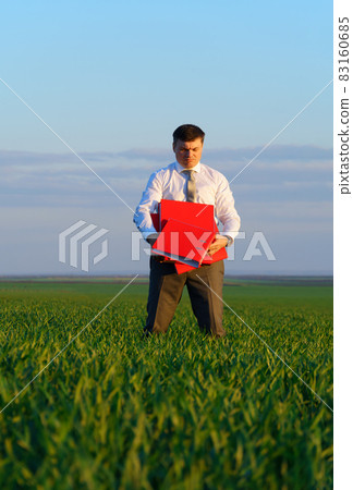 businessman holds an office red folder with documents in a green grass field - business concept businessman holds an office red folder with documents in a green grass field - business concept 83160685