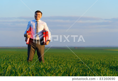 businessman holds an office red folder with documents in a green grass field - business concept businessman holds an office red folder with documents in a green grass field - business concept 83160690