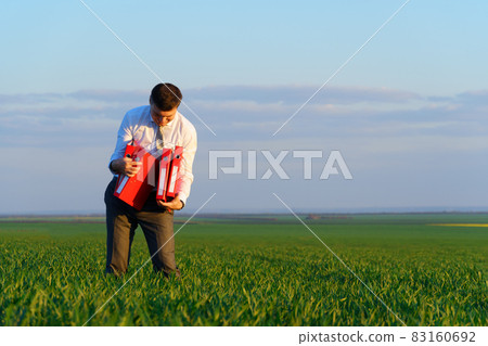 businessman holds an office red folder with documents in a green grass field - business concept 83160692