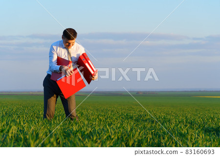 businessman holds an office red folder with documents in a green grass field - business concept businessman holds an office red folder with documents in a green grass field - business concept 83160693