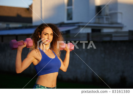 portrait of a woman with copy space leventando dumbells with blue clothes and beautiful golden light portrait of a woman with copy space leventando dumbells with blue clothes and beautiful golden light 83161380