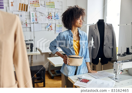 Thoughtful African-American woman leans into table with drawings and sewing machine Thoughtful African-American woman leans into table with drawings and sewing machine 83162465