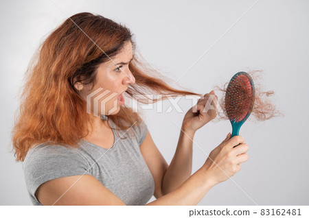 Caucasian woman with a grimace of horror holds a massage comb with a bun of hair. Hair loss and female pattern baldness. Caucasian woman with a grimace of horror holds a massage comb with a bun of hair. Hair loss and female pattern baldness. 83162481