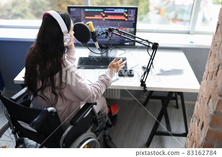 Woman in wheelchair with headphones speaks into microphone in front of computer monitor Woman in wheelchair with headphones speaks into microphone in front of computer monitor 83162784