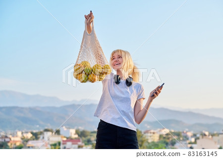 A female teenager with an eco-friendly mesh bag of farm organic oranges 83163145
