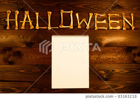 Lettering from the bones of the word Halloween and blank sheet of paper on a dark brown wooden background. Design to celebrate Halloween day. Happy Halloween. Scary inscription. Copy space for text Lettering from the bones of the word Halloween and blank sheet of paper on a dark brown wooden background. Design to celebrate Halloween day. Happy Halloween. Scary inscription. Copy space for text 83163218