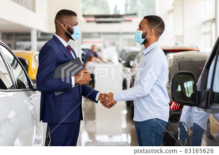 Car Dealership. Black Salesperson In Medical Mask Shaking Hands With Male Customer Car Dealership. Black Salesperson In Medical Mask Shaking Hands With Male Customer 83165626