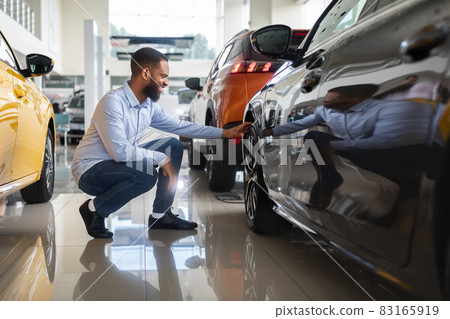 Black Male Customer Choosing New Automobile In Dealership Center, Examining Wheel Rims 83165919