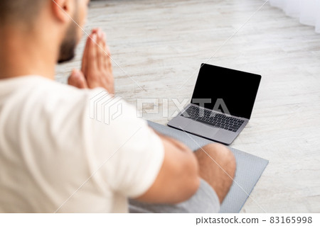 Unrecognizable young Arab man meditating or doing yoga in front of laptop computer with blank screen at home, mockup Unrecognizable young Arab man meditating or doing yoga in front of laptop computer with blank screen at home, mockup 83165998