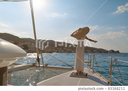 Beautiful woman wearing straw hat and white dress on a yacht enjoys the journey, Spetses, Greece, Europe 83168211